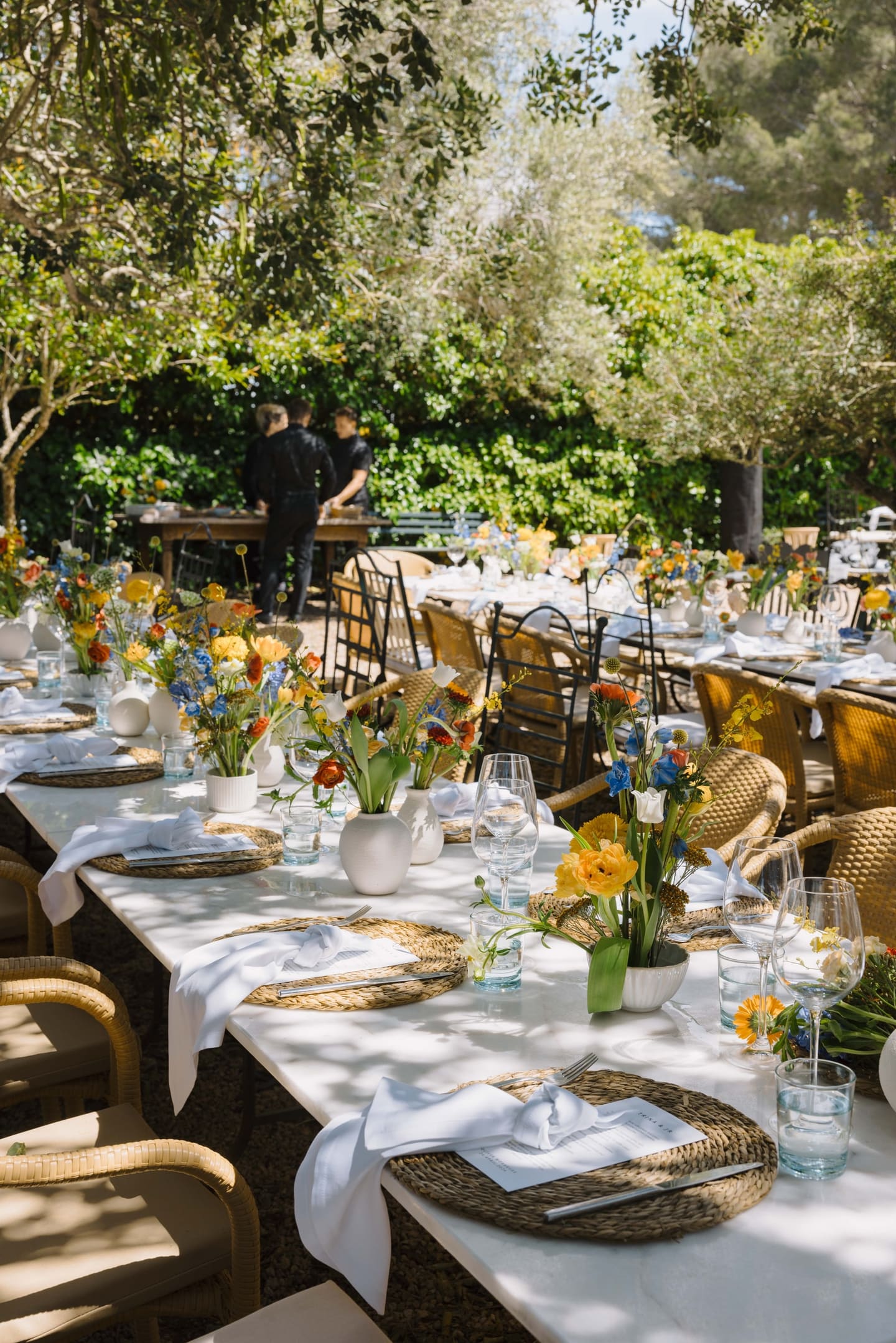 A colourful table setting with blue and yellow flowers beneath a tree