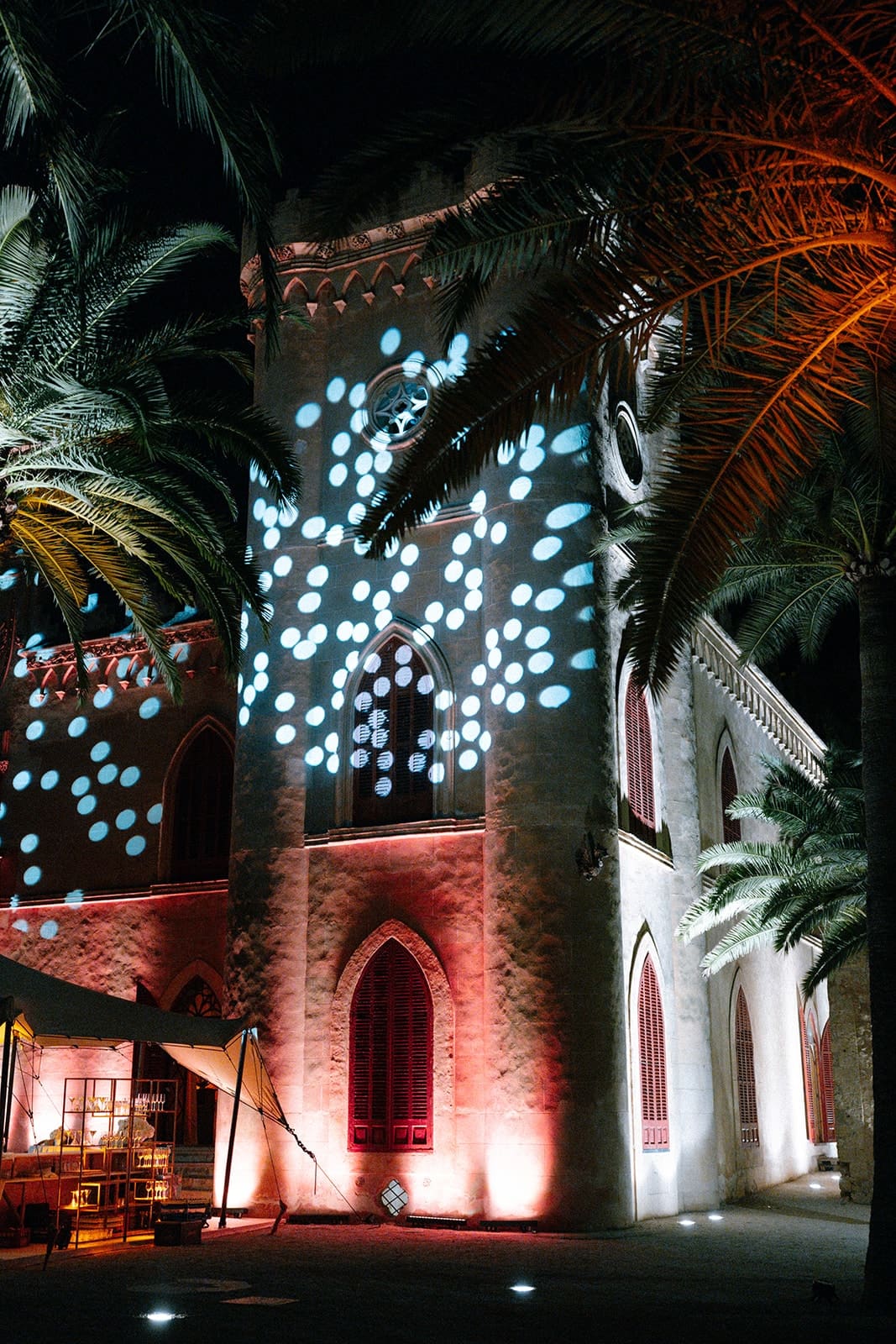 A Mallorcan facade and palm trees lit with a projection of white light at night