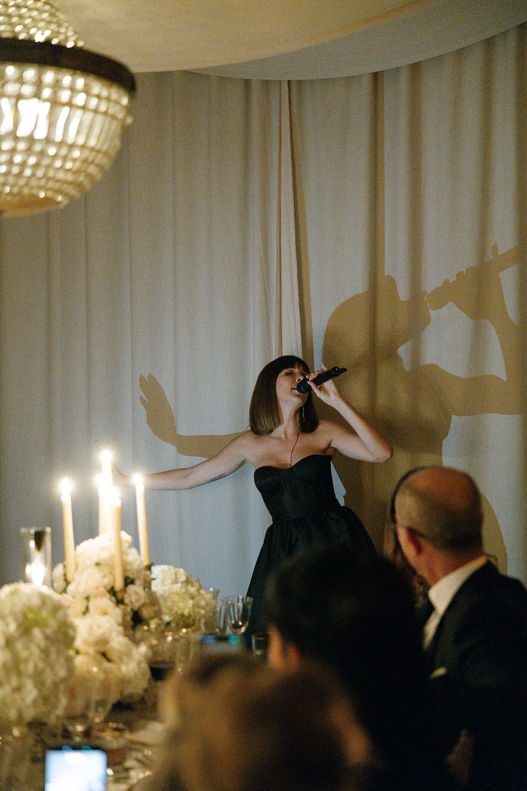 A singer performing by candlelight in front of a draped wall