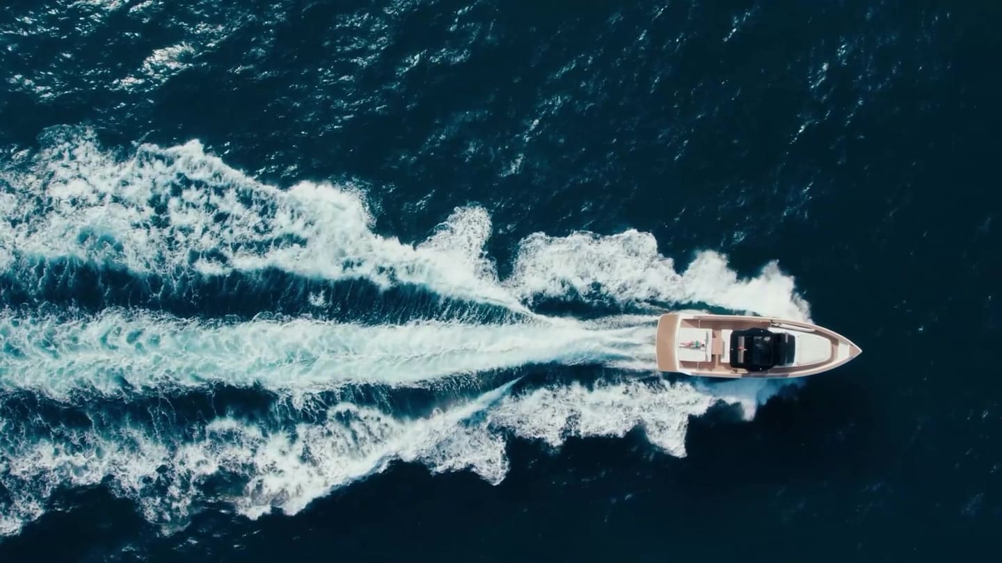 A yacht seen from above, cutting a white wake across deep blue Mediterranean water off Mallorca