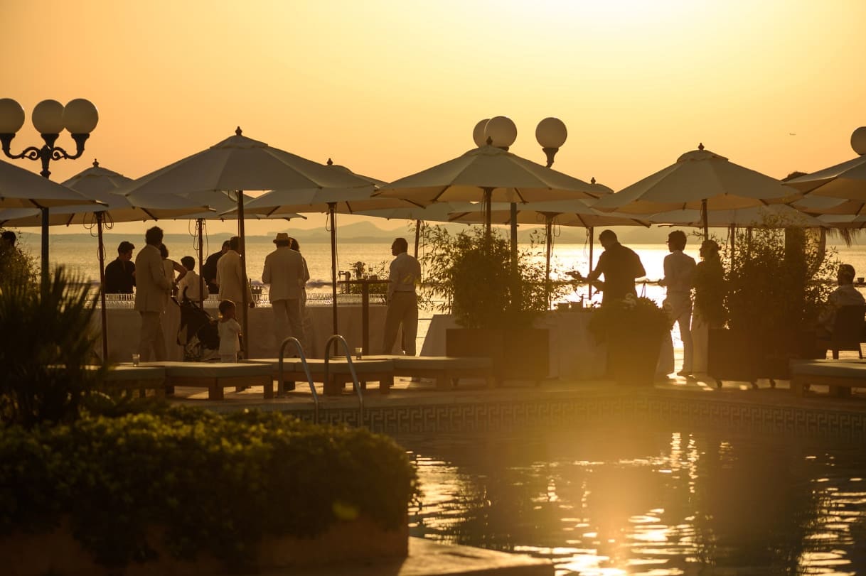Guests on a beach club terrace at sunset with parasols silhouetted against the sea