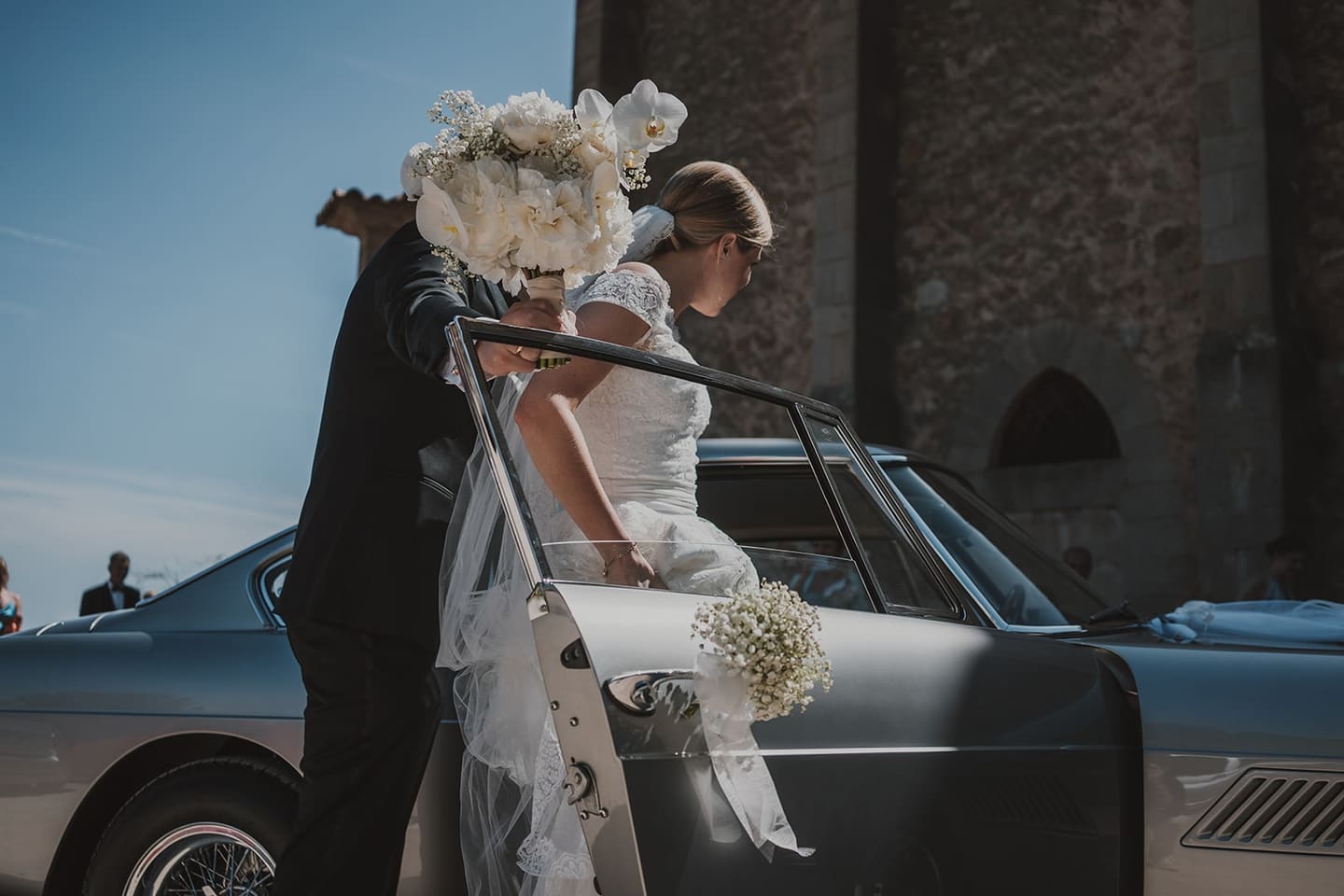 A bride stepping out of a classic car in front of a stone building
