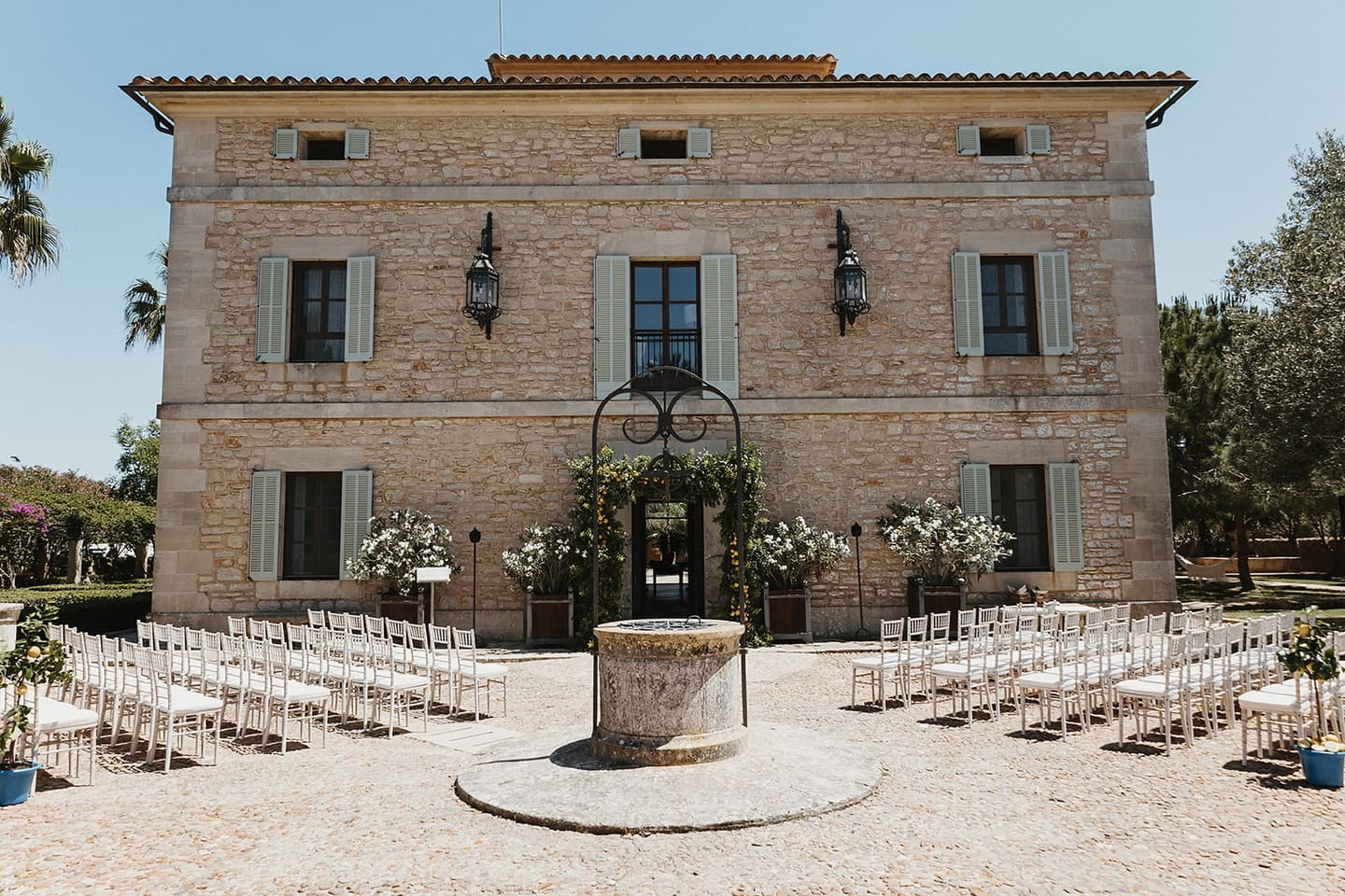Rows of ceremony chairs in front of a Mallorcan finca with a stone well