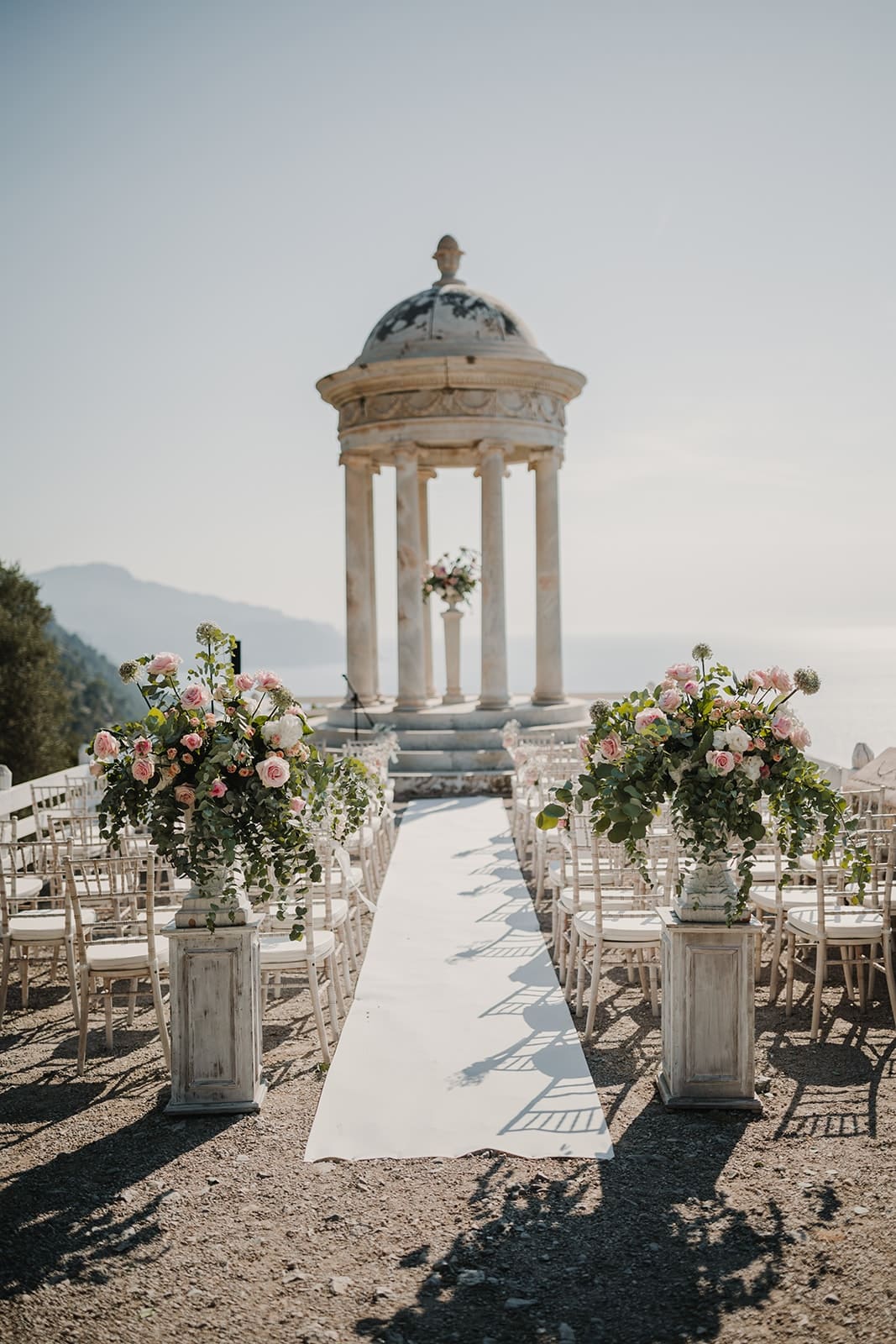 A wedding ceremony set inside a stone temple above the sea, framed by pink and white flowers