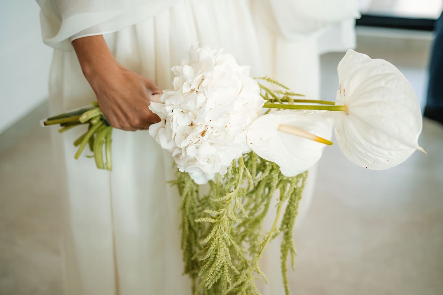 A hand holding a white bouquet of orchids and anthuriums